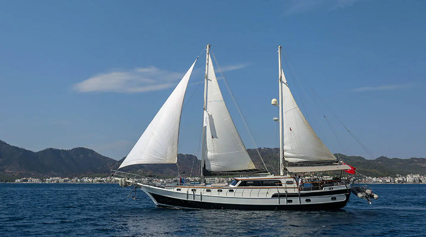 Grand Sailor yacht with white sails sailing on calm blue sea at sunset