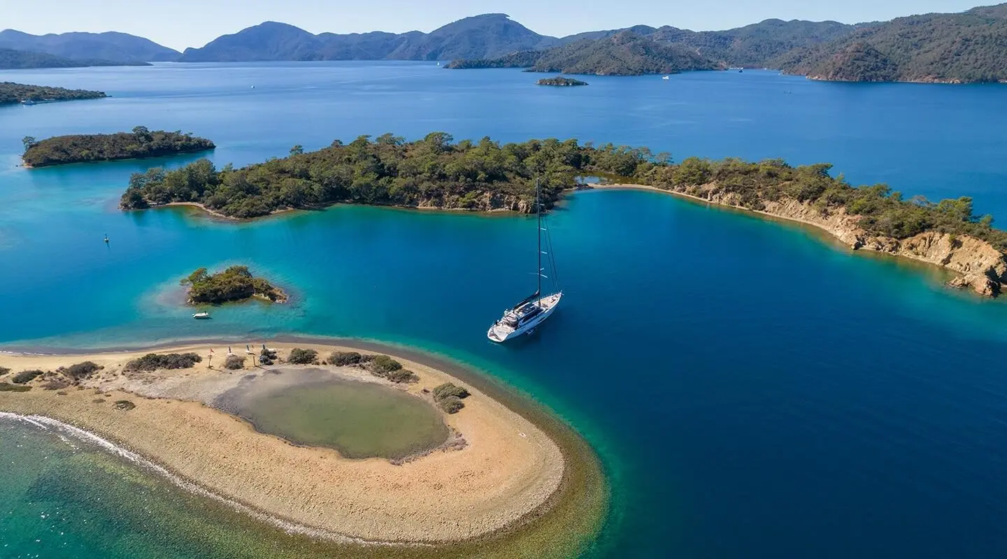Sailboat anchored near a green island and sandy shoreline