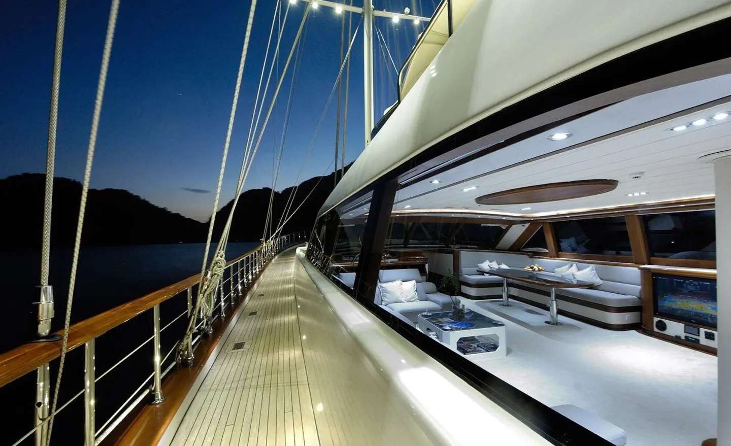 Sunlit yacht Alessandro I deck with polished wood, lines, and seating along port side