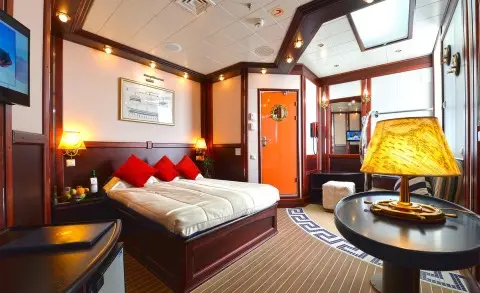Interior of yacht Running on Waves with a bed, red pillows, and warm lighting