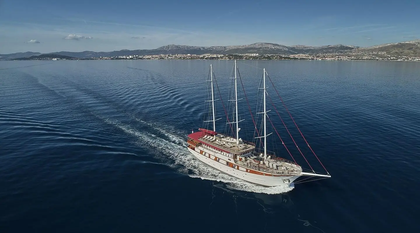 A red-sailed luxury sailing yacht Amorena glides on calm blue ocean waters
