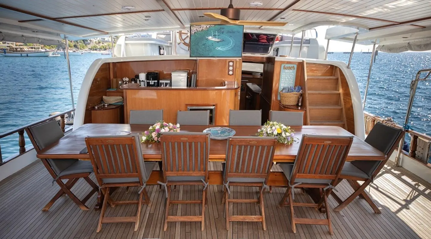 Wooden dining table with chairs on the deck, bar area behind, sea view