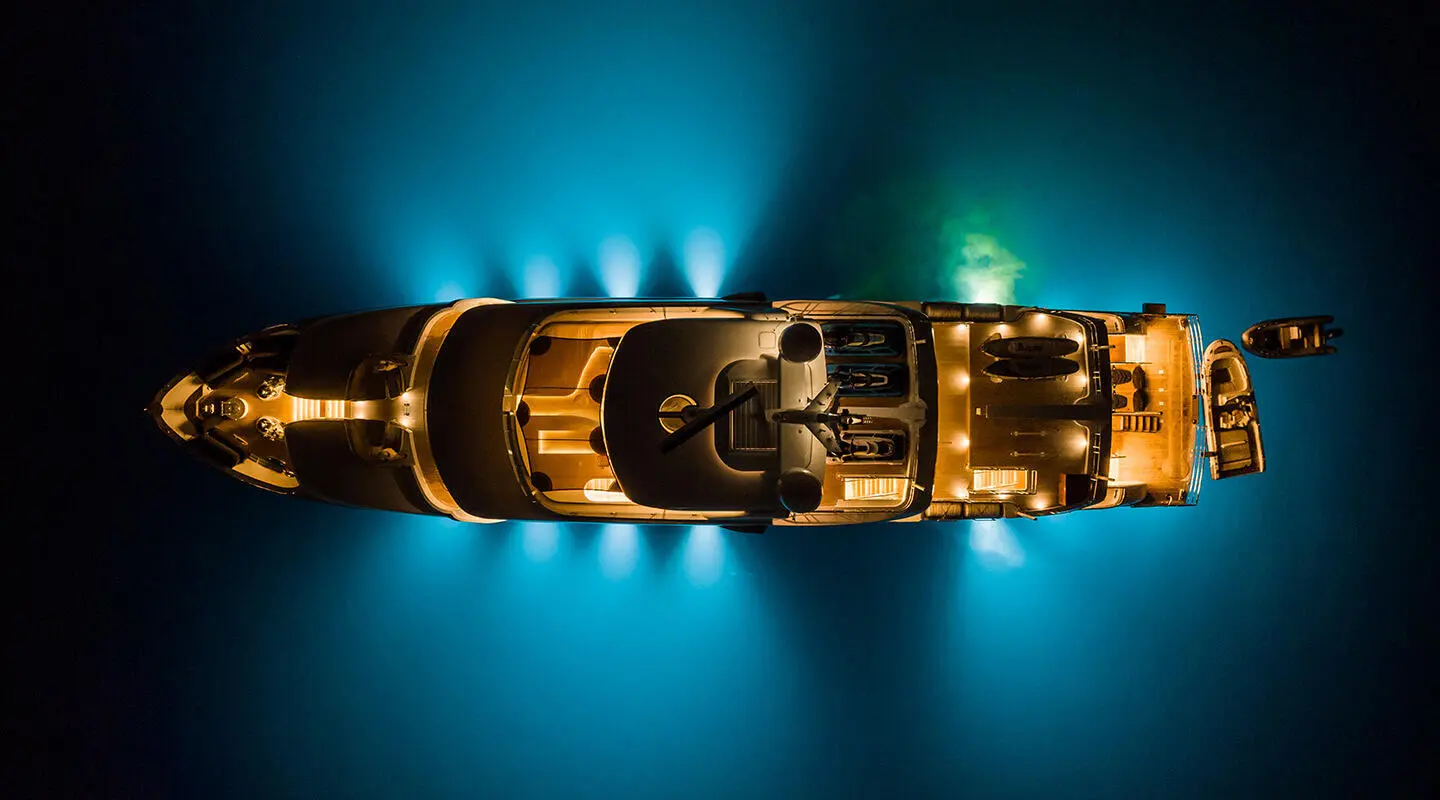Top-down night view of Serenity yacht glowing blue in water, amber lights