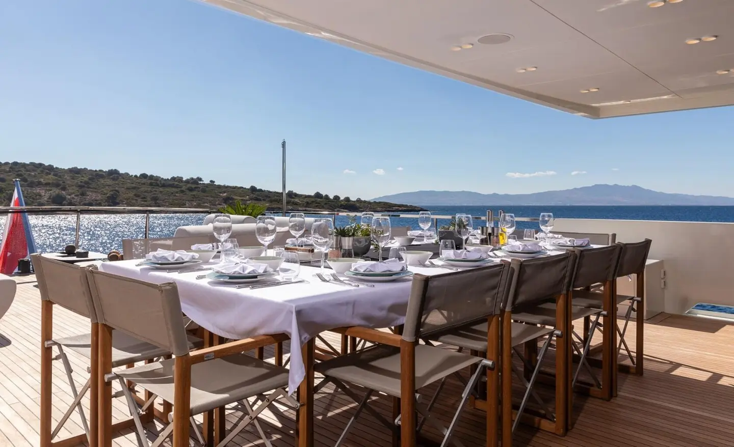 Large on-deck dining table set with white linens and glassware on a yacht