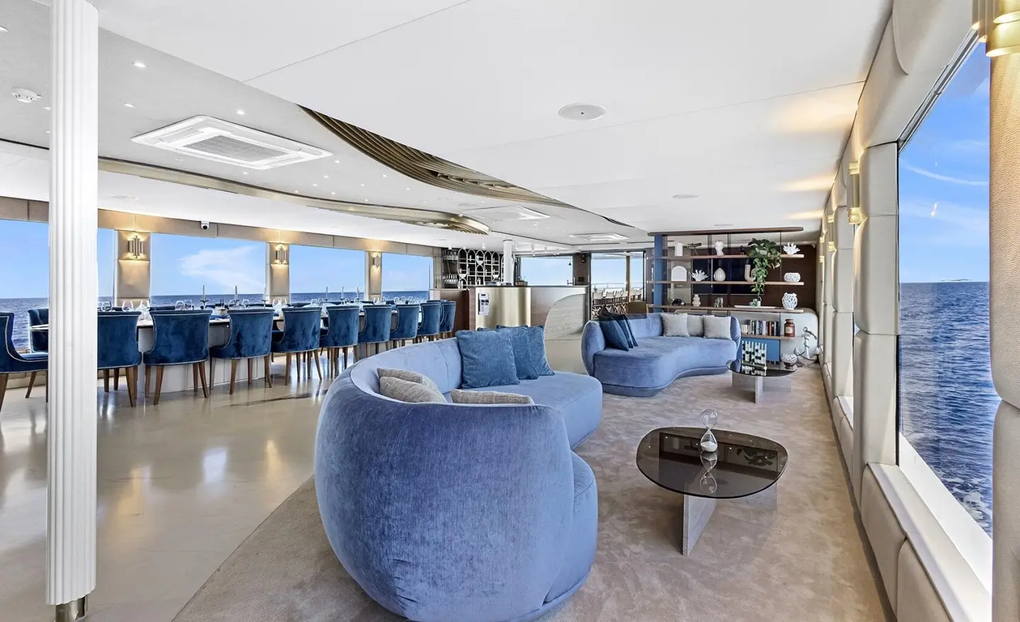 Spacious yacht Bella salon with blue chairs, white counters, and large windows