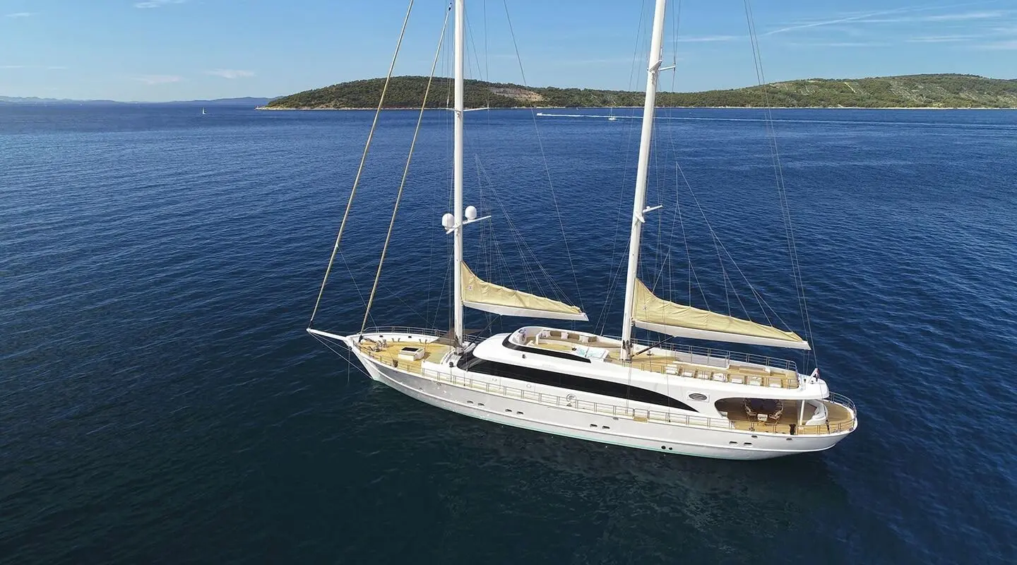 A sleek sailing yacht named Acapella glides on calm blue waters with sails down