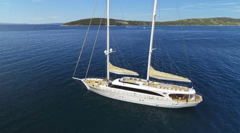 A sleek sailing yacht named Acapella glides on calm blue waters with sails down
