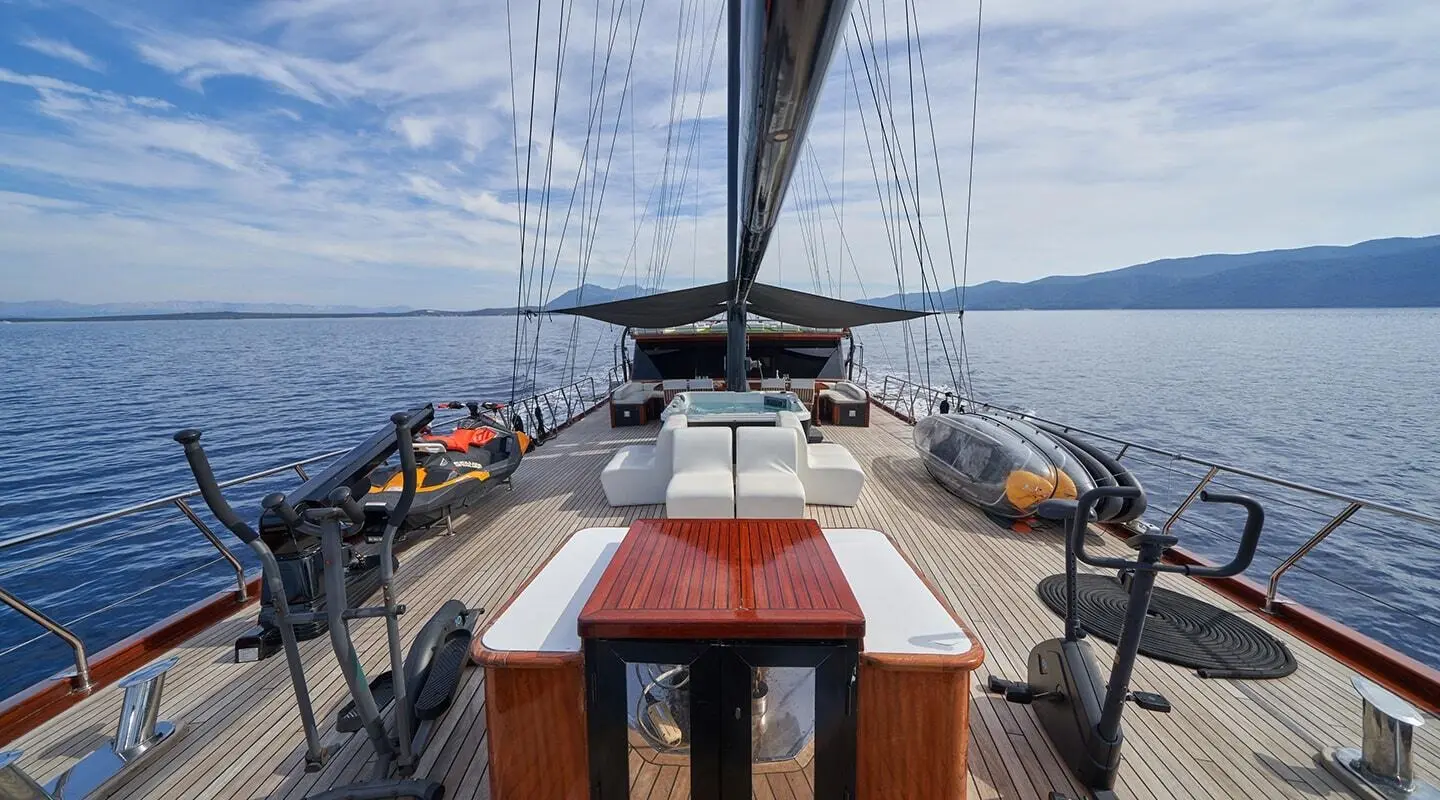 Stella Maris yacht deck view with wooden helm and sailing rig at sunset
