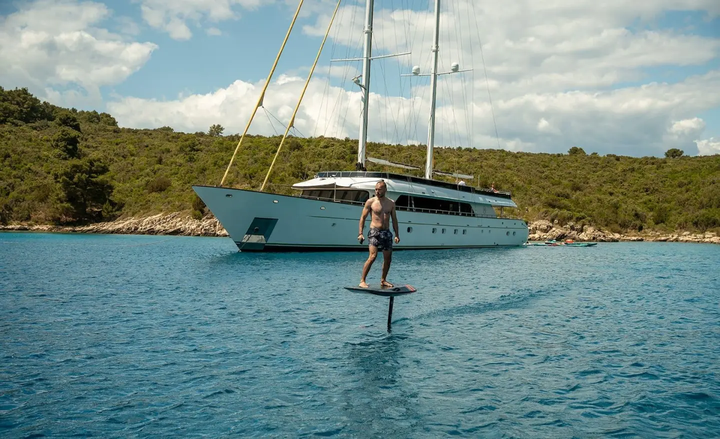 Yacht named Anima Maris anchored in calm turquoise water with a person on a padel board nearby
