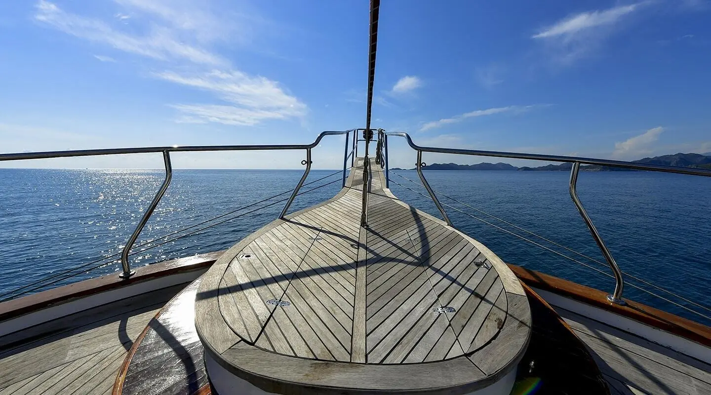 Blu Dream yacht bow deck with teak planks and stainless railings on calm sea