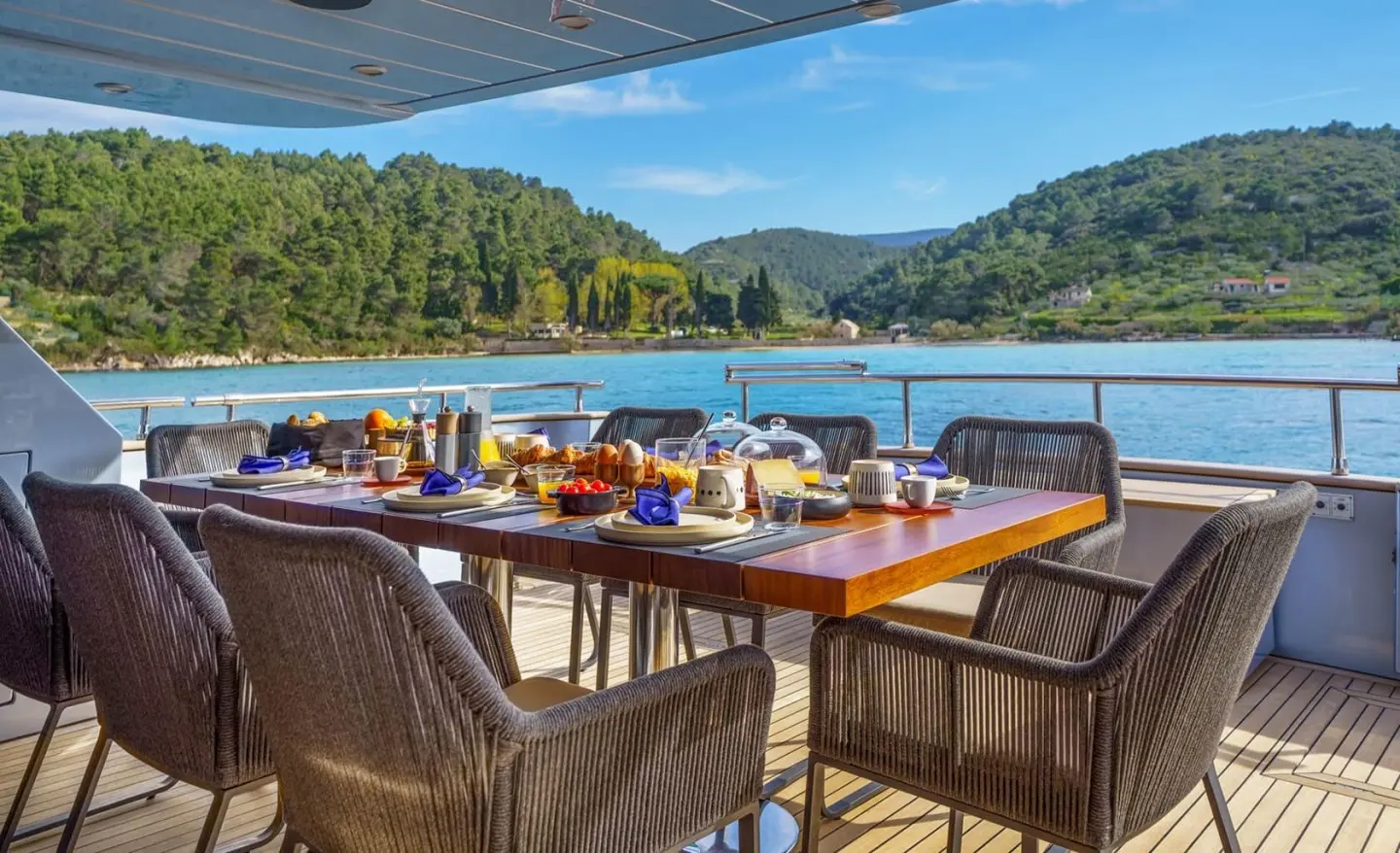 Phantom yacht dining area at sunset with wooden table, chairs, and sea view