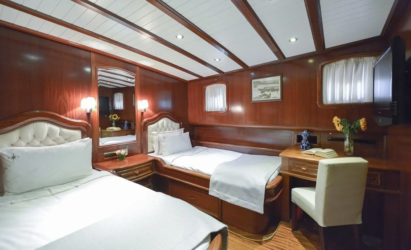 Interior of Lady Christa yacht: wood paneling, two beds, seating area, porthole windows, warm lighting