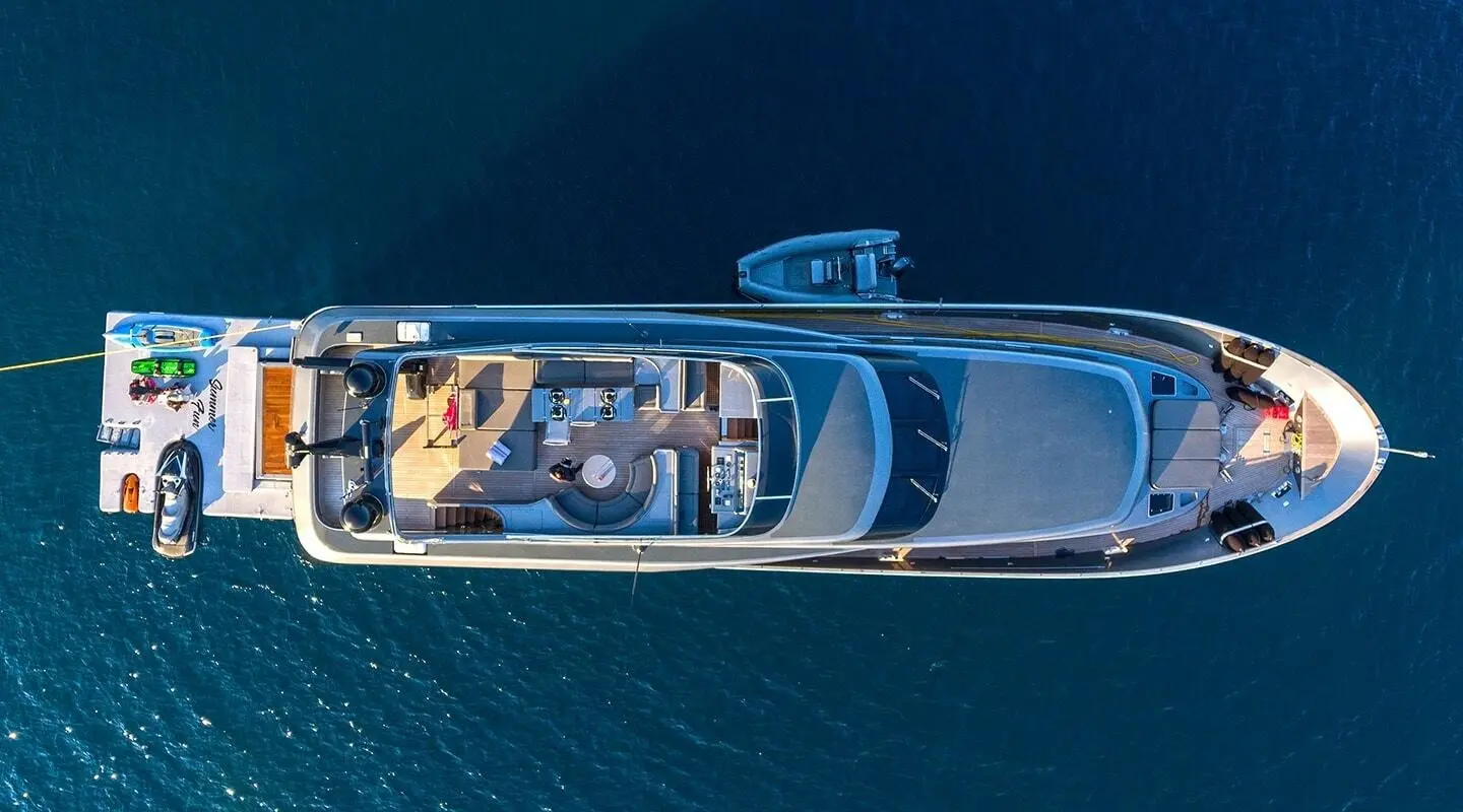 Top-down view of a small luxury sailing yacht on calm blue water with white deck and seating areas
