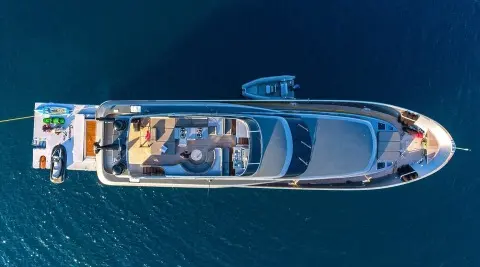 Top-down view of a small luxury sailing yacht on calm blue water with white deck and seating areas