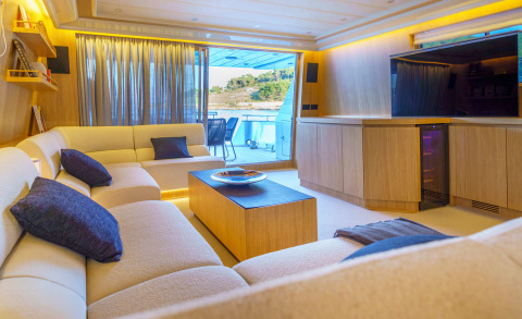Light-colored L-shaped sofa in a yacht salon with a wooden coffee table and view of the deck outside through glass doors