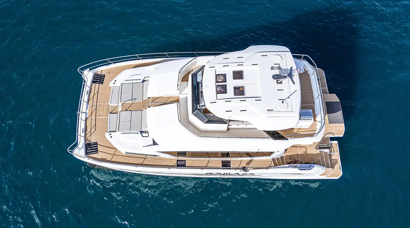 Top-down view of a white By My Side yacht with teak deck cruising in blue sea