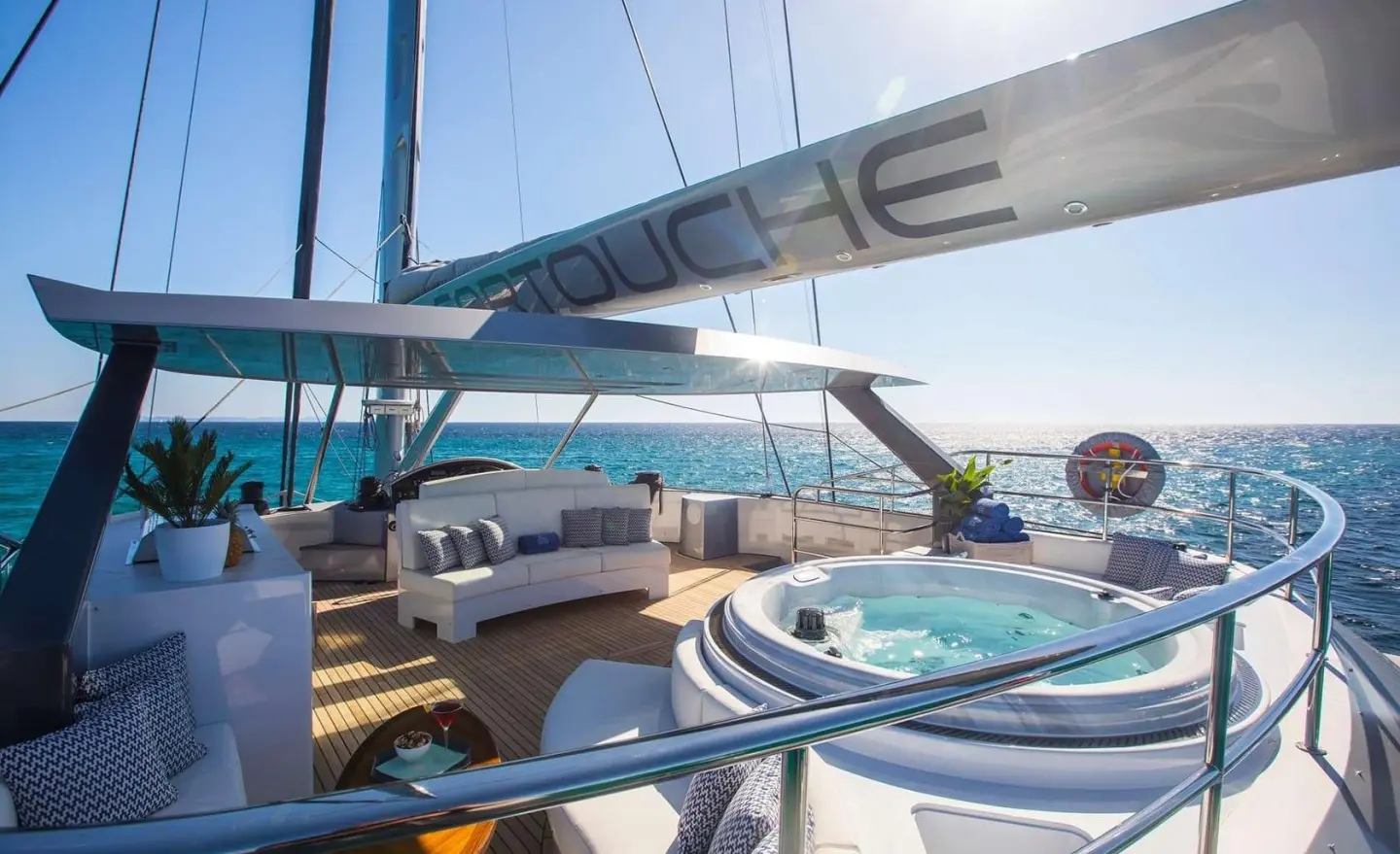 Sunlit open sea deck with white seating area and a round jacuzzi on a luxury yacht