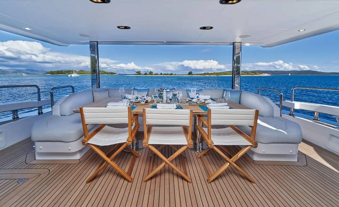 Aft deck of Aluminia Too with wooden chairs and blue sea backdrop