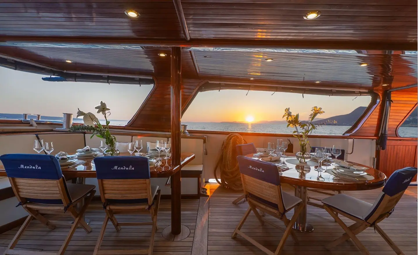 Sunset view from a yacht's deck with seating and rigging silhouettes
