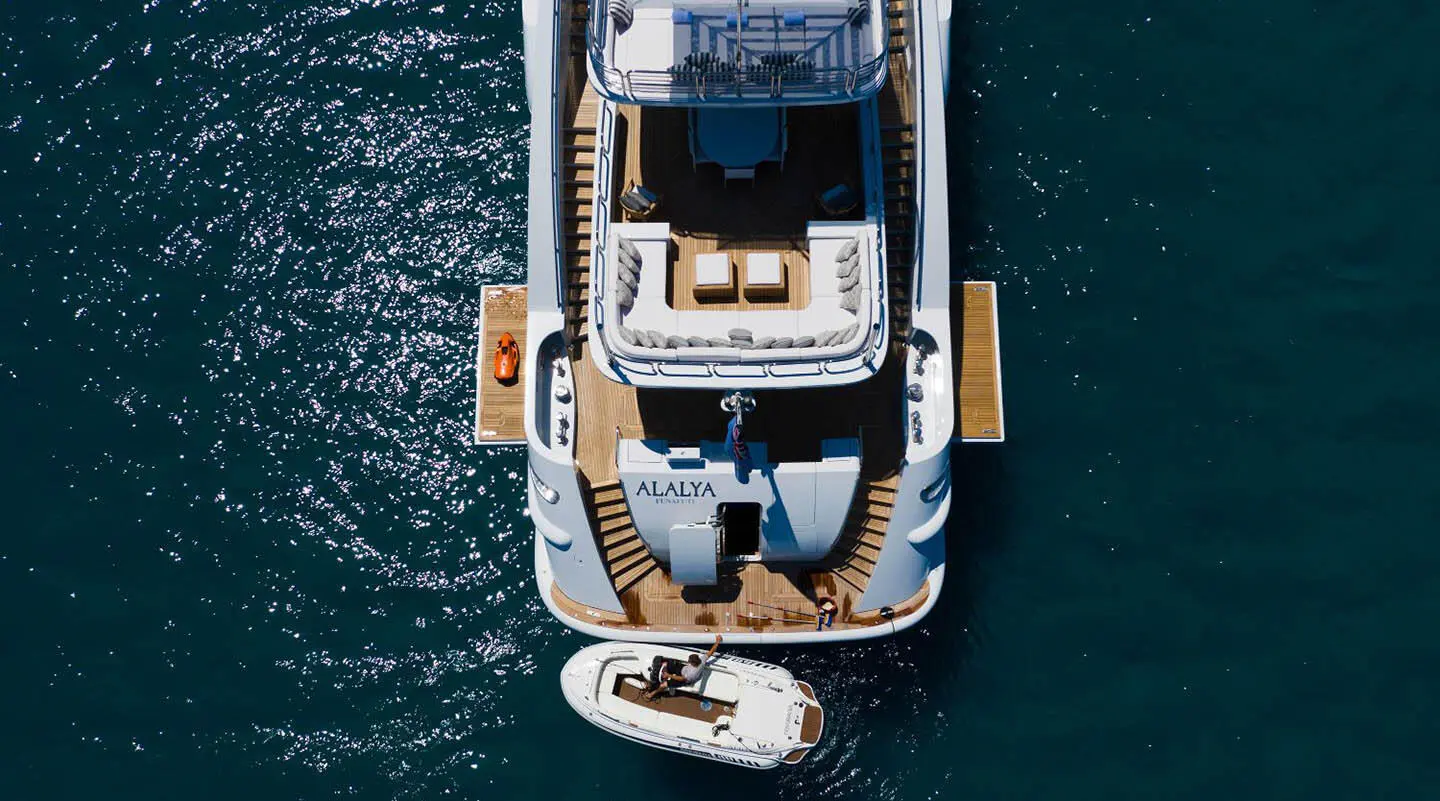 Aerial view of the Alalya yacht with sunlit deck and tender anchored nearby