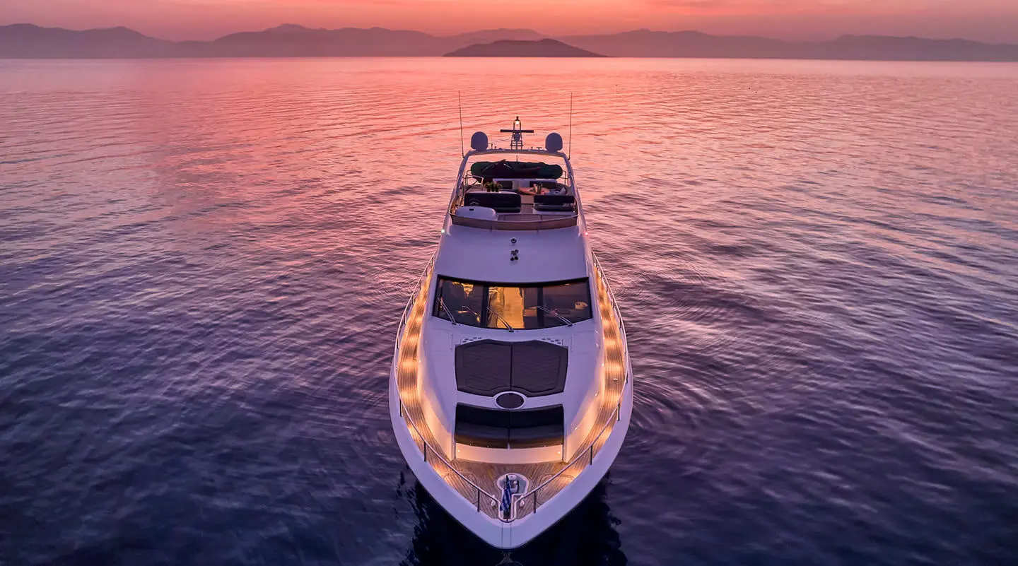 Top-down shot of a sleek white and blue yacht anchored on calm water at sunset