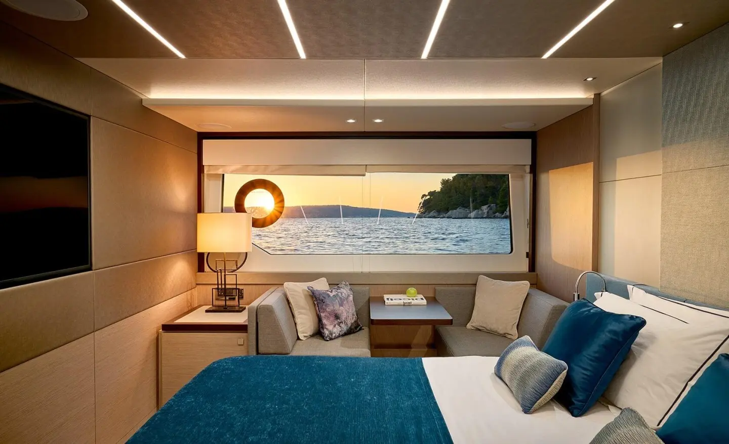 Cozy yacht bedroom with blue bedspread, cushions, and porthole window view