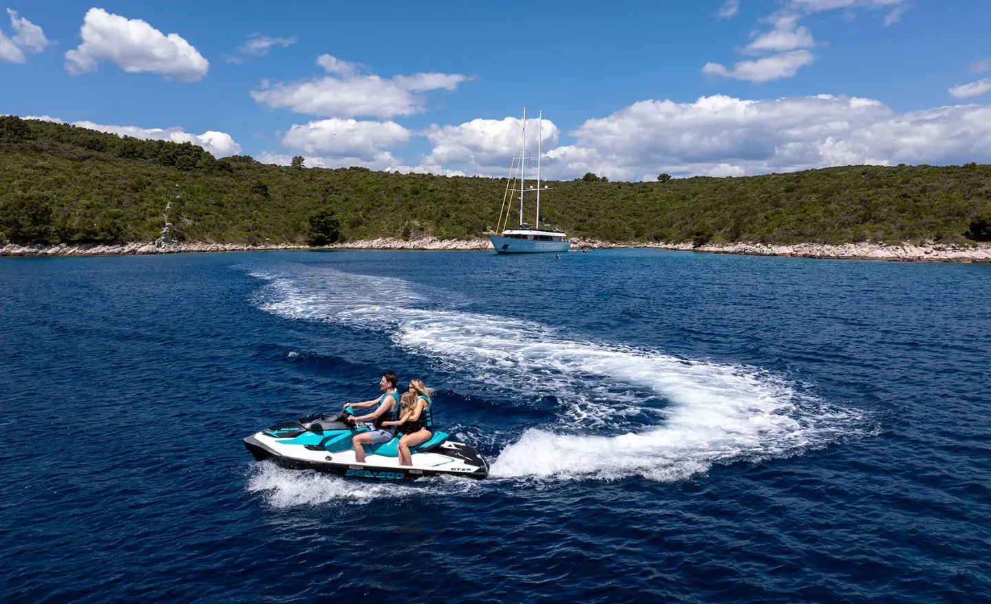 Anima Maris yacht on blue water with a person riding a jetski creating white wake