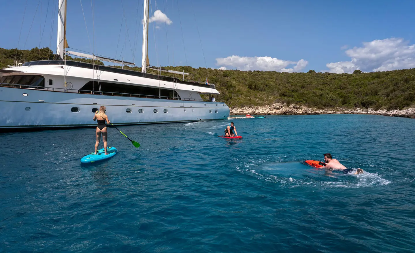 Yacht Anima Maris anchored near shore with people swimming and paddling in turquoise water