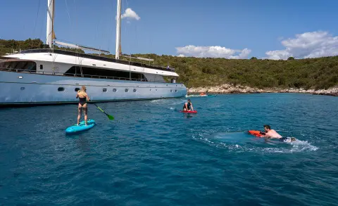 Yacht Anima Maris anchored near shore with people swimming and paddling in turquoise water