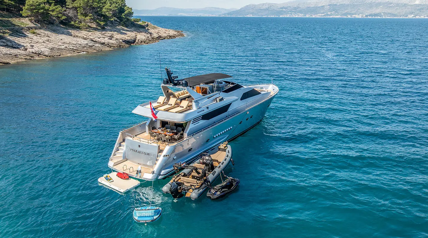 Phantom yacht anchored at sea during sunrise, calm blue water, small boat nearby