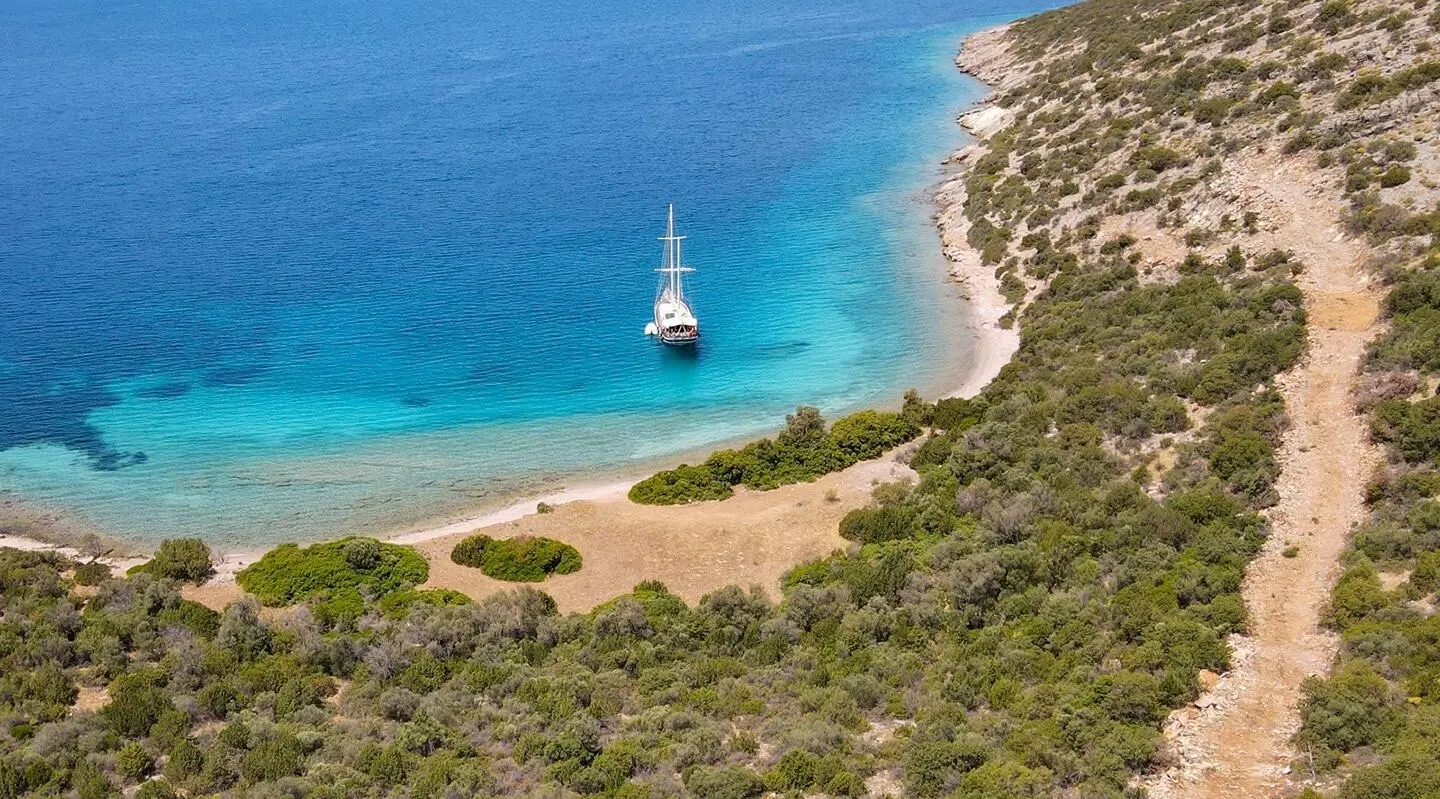 A luxury gulet sailing at sunset near a rocky coastline and clear blue water