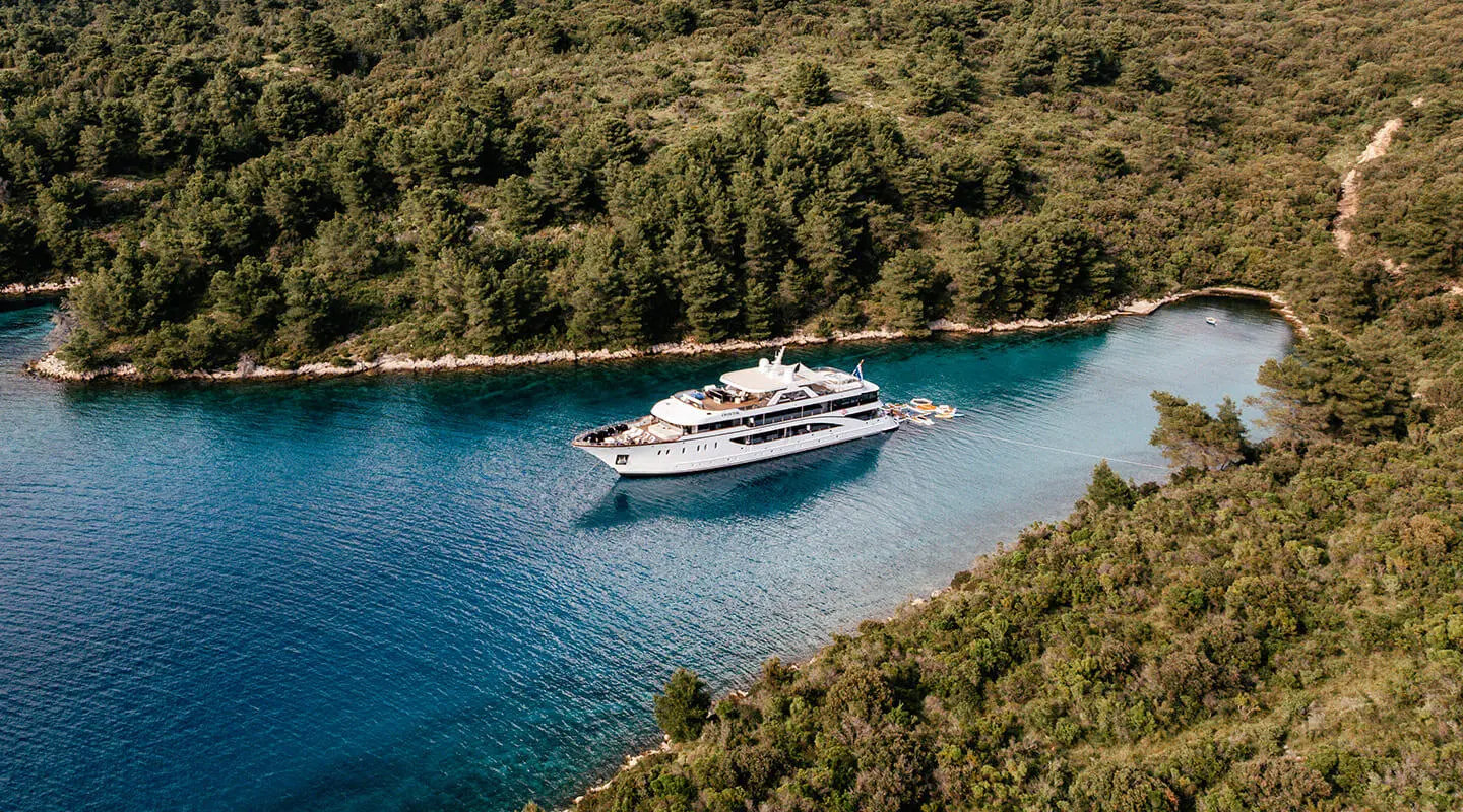 White luxury motor yacht Cristal anchored in a forested bay