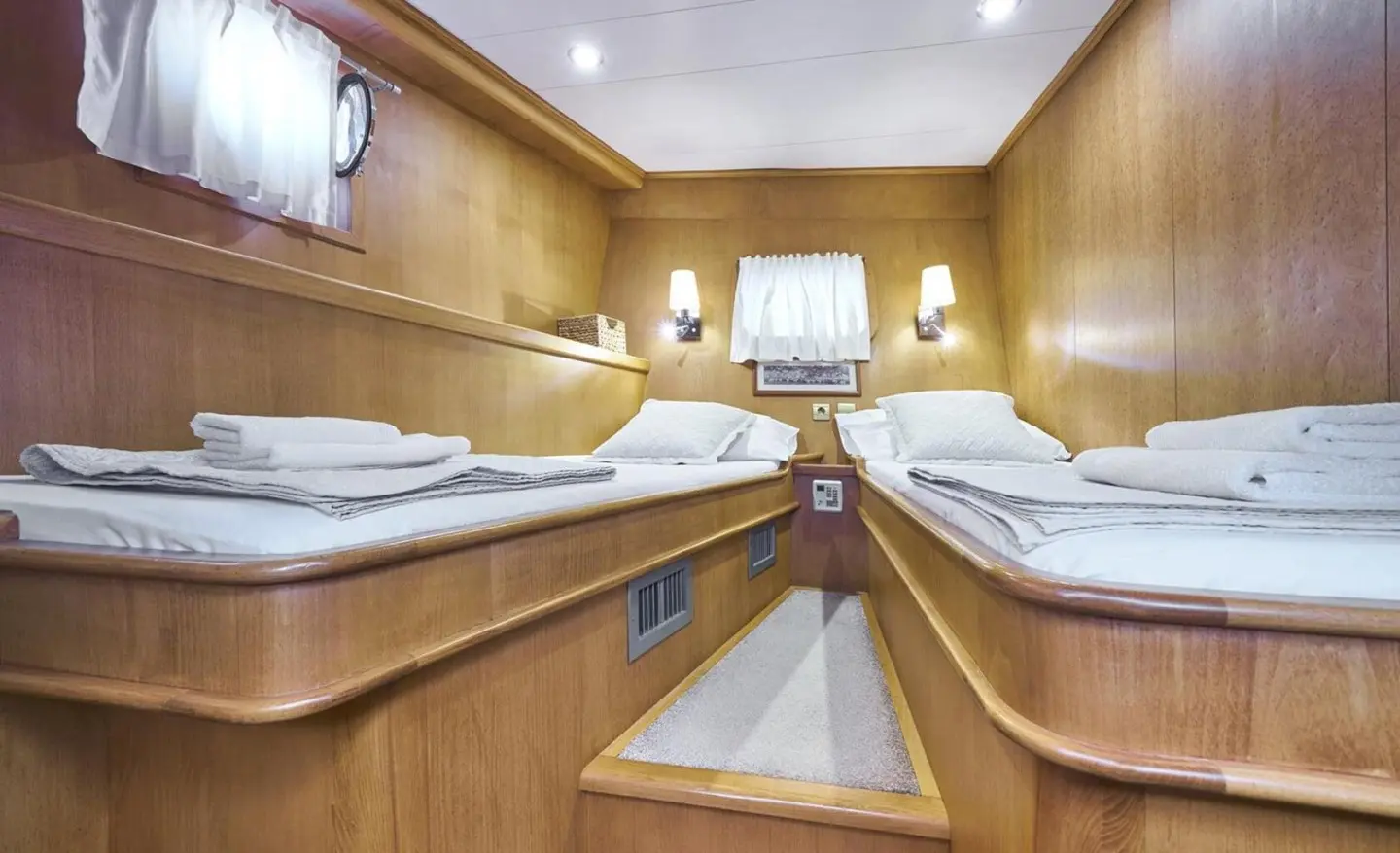 Interior of a wooden yacht cabin with bunks and porthole view
