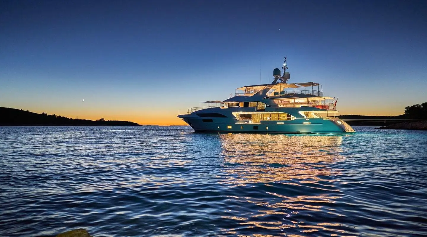 Happy Me yacht cruising at sunset with illuminated exterior and calm blue sea