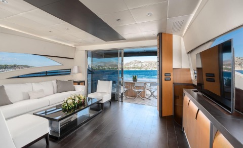 Interior of One yacht: white leather sofa, glass coffee table, modern lighting, and open balcony to blue sea and hills