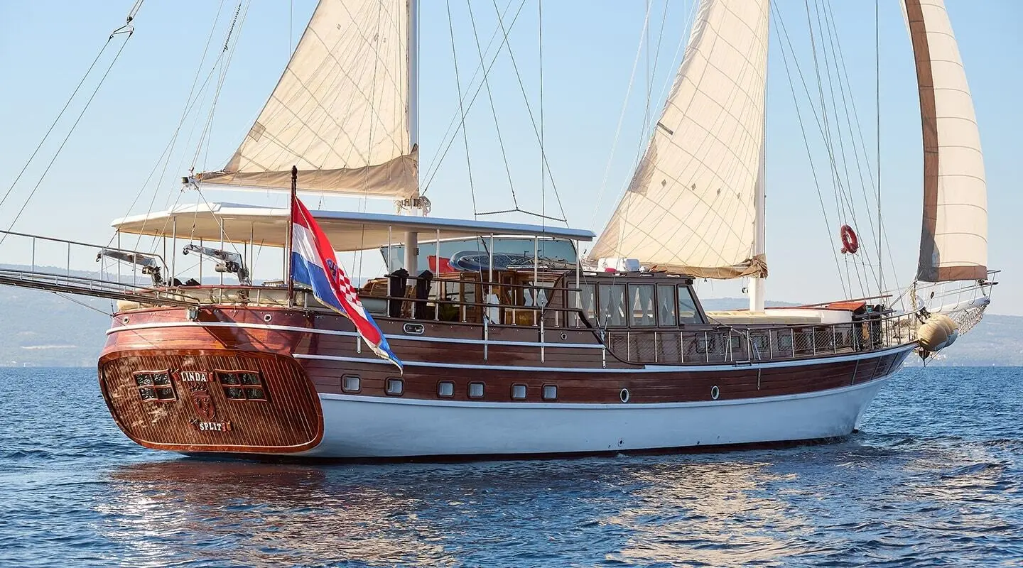 Linda yacht with white sails and passengers on deck at sunset harbor