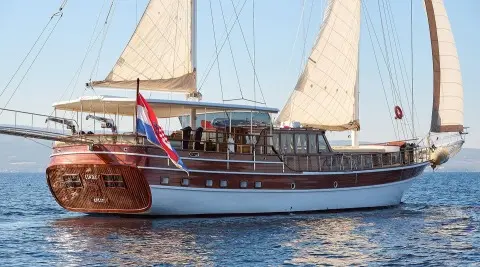 Linda yacht with white sails and passengers on deck at sunset harbor