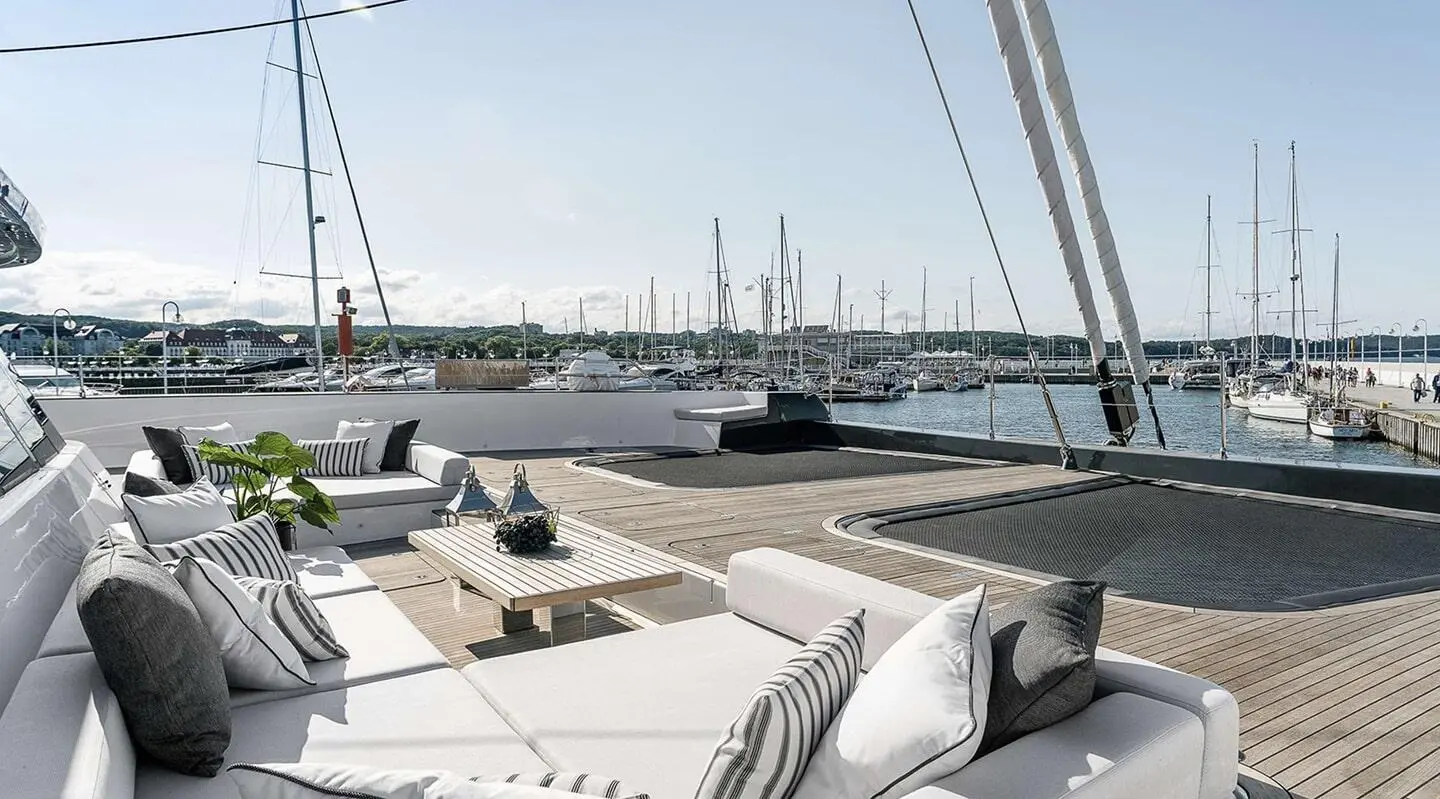 Yacht deck with seating and sails, harbor with moored boats in sunset