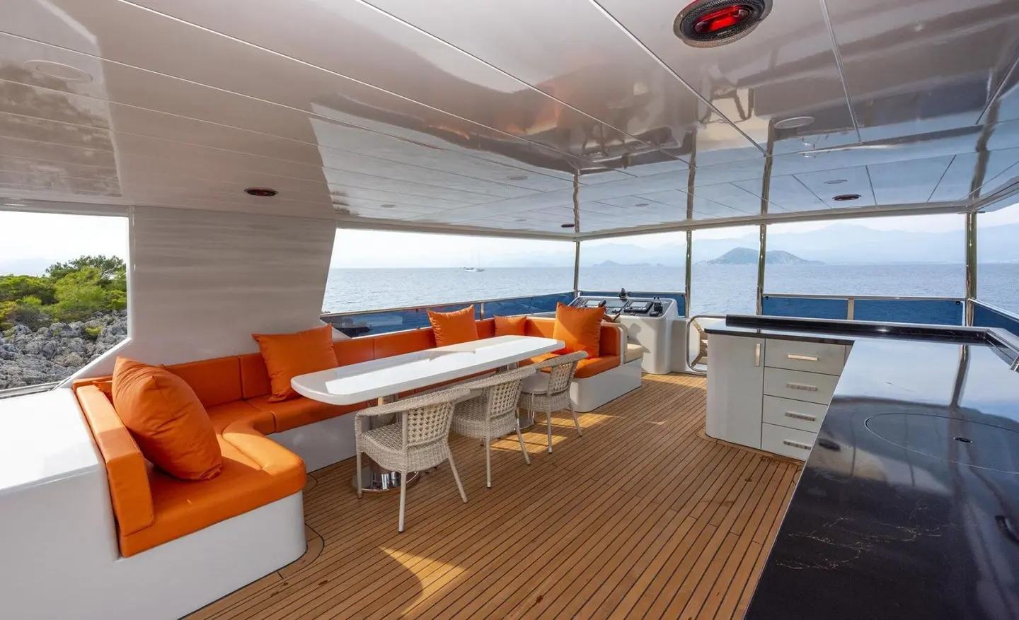 Covered yacht cockpit with orange seating, white table, wood deck, and blue ocean view