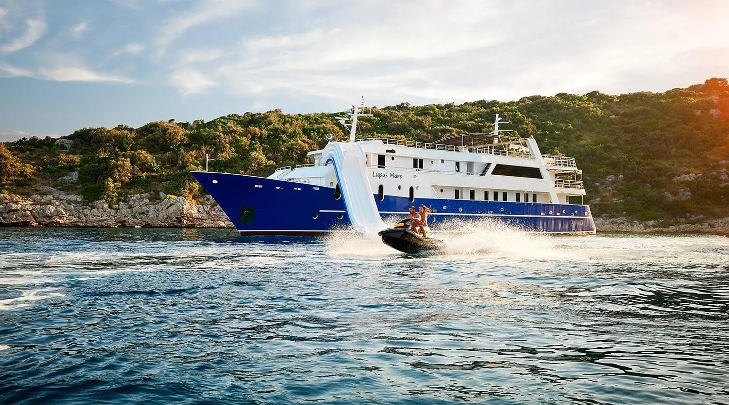 Blue Lupus Mare yacht near a dock with water and hills in background