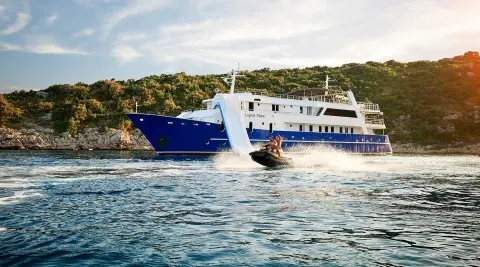 Blue Lupus Mare yacht near a dock with water and hills in background
