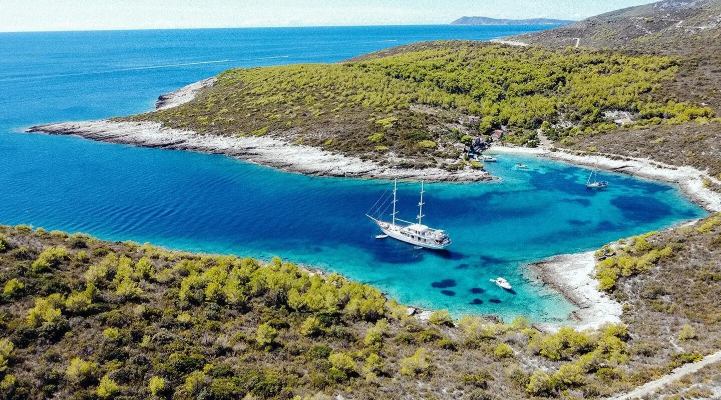 Corsario yacht anchored in a turquoise cove, a pristine bay surrounded by rocky coastline