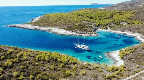 Corsario yacht anchored in a turquoise cove, a pristine bay surrounded by rocky coastline