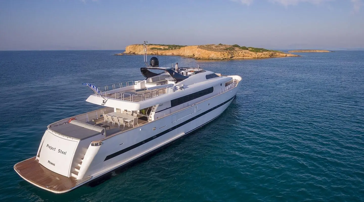 White luxury motor yacht in open sea with rocky island in background