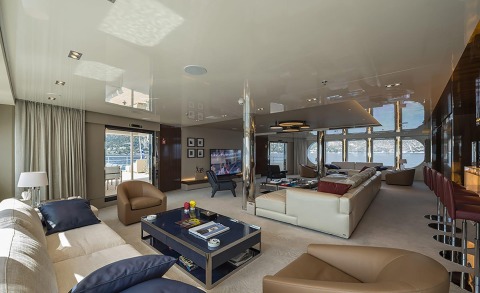 Marquise luxury yacht interior: open-plan lounge with cream sofas, brown chairs, glass coffee table, bar stools, and panoramic windows overlooking the water