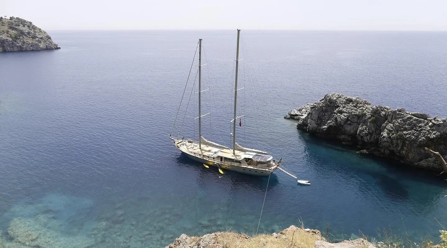 Sailing yacht anchored in clear blue water by rocky shore