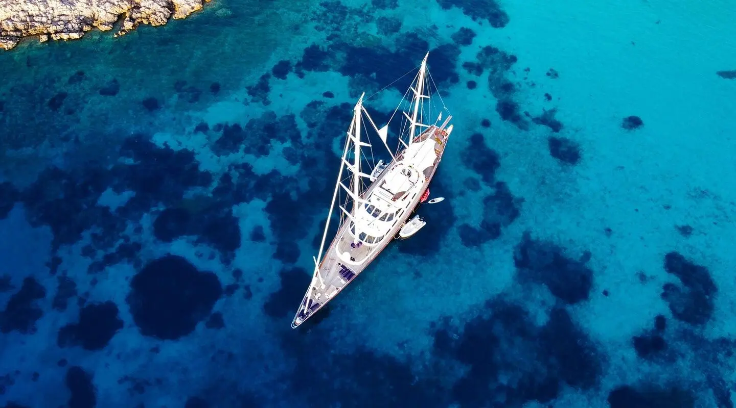Top-down view of a sleek white sailing yacht anchored in bright turquoise water