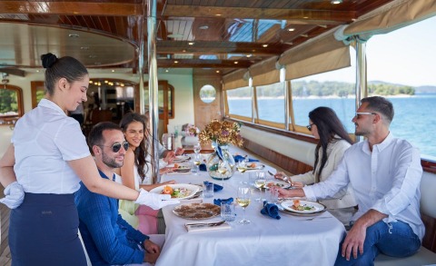 People dining on the outdoor deck of a yacht with sea view and sunset table setting