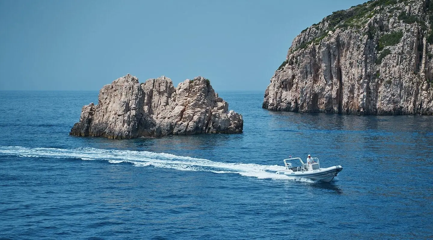 La Perla yacht anchored in blue sea with rock formations nearby