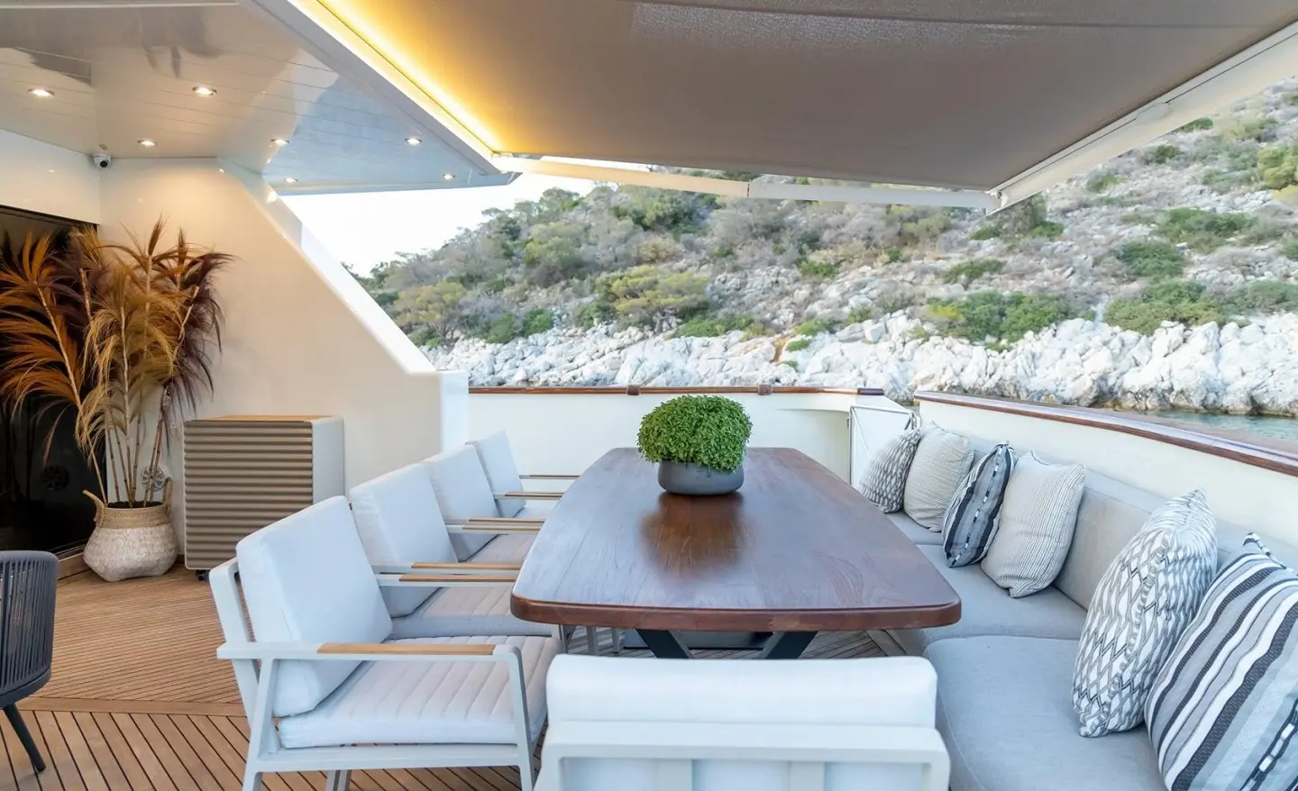 Aquila yacht deck dining area with a long wooden table and cushioned seating